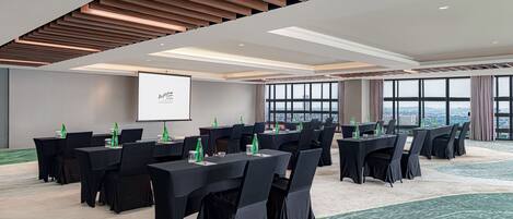 Un salón de conferencias con varias mesas, sillas y una pantalla para proyector.