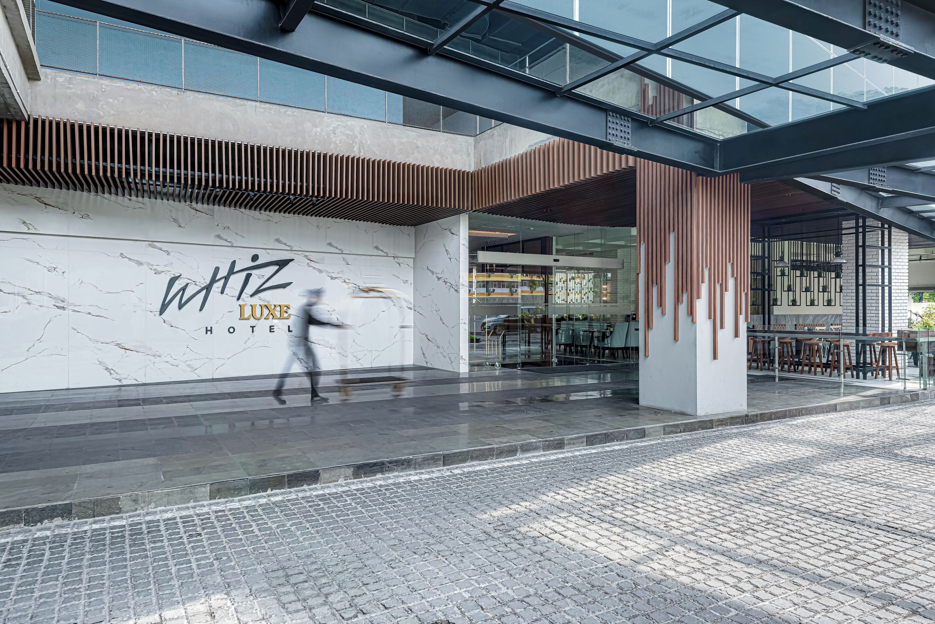 Une entrée d’hôtel moderne, avec un mur en marbre et une enseigne indiquant « WHIZ LUXE HOTEL ».