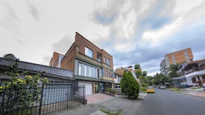En bostadsgata med ett tvåvåningshus som har ett garage, en liten trädgård framför huset med ett träd och en parkerad bil.
