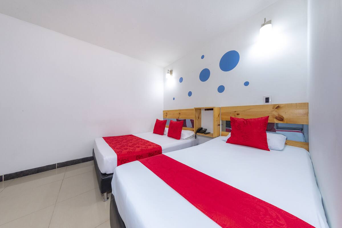 Ein Hotelzimmer mit zwei Betten, jeweils mit roter Bettdecke und Kissen, und einem Holzkopfstück.