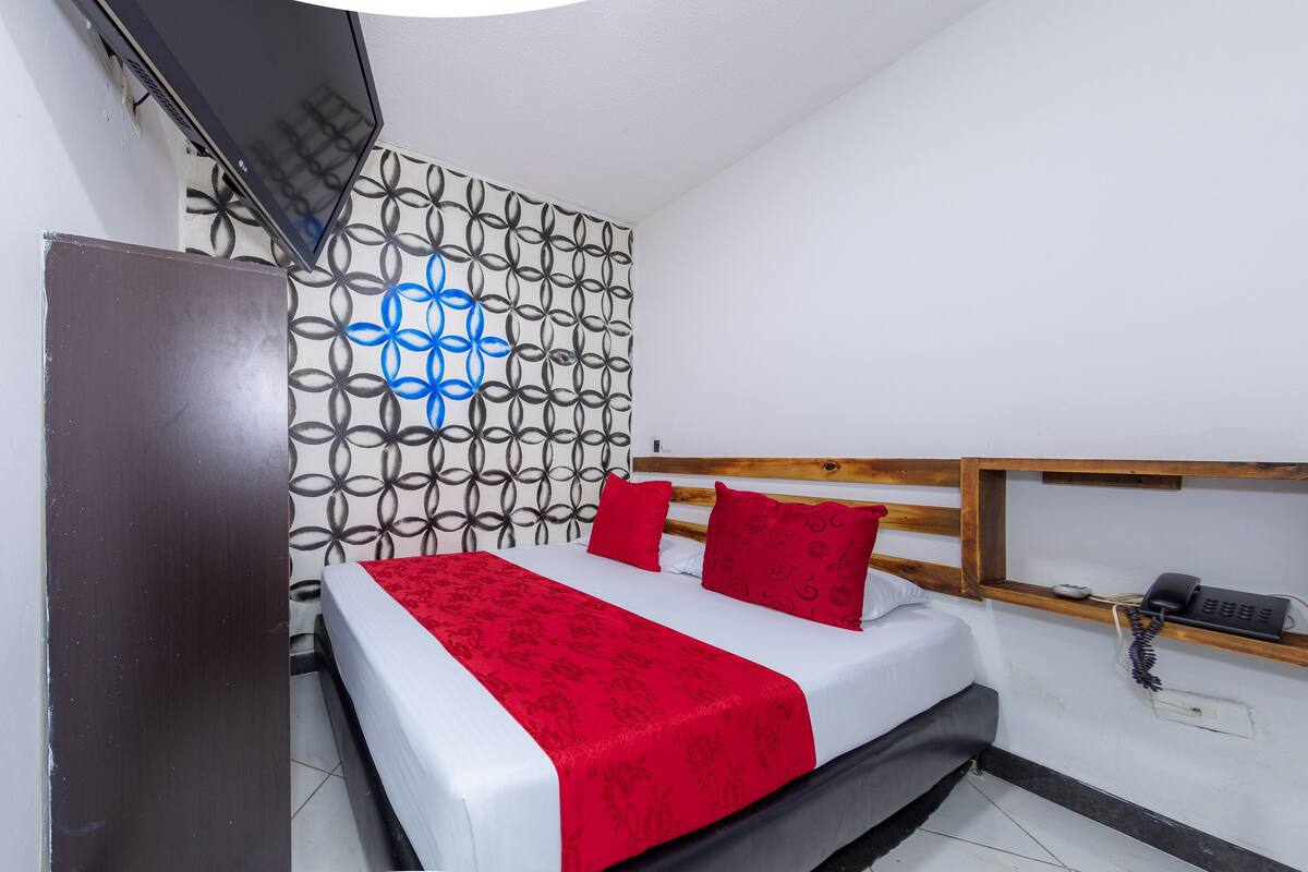 Ein Hotelzimmer mit Bett, Holz-Kopfteil, roter Bettdecke, Wand mit Muster und Telefon auf einem Regal.