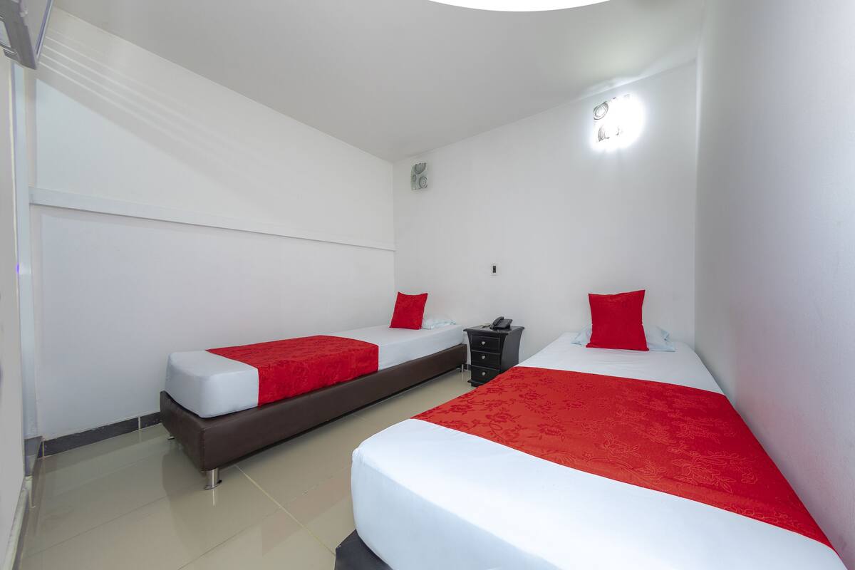 Ein Hotelzimmer mit zwei Einzelbetten, jeweils mit einer roten und weißen Tagesdecke, einem kleinen Nachttisch mit Telefon und einer wandmontierten Lampe.