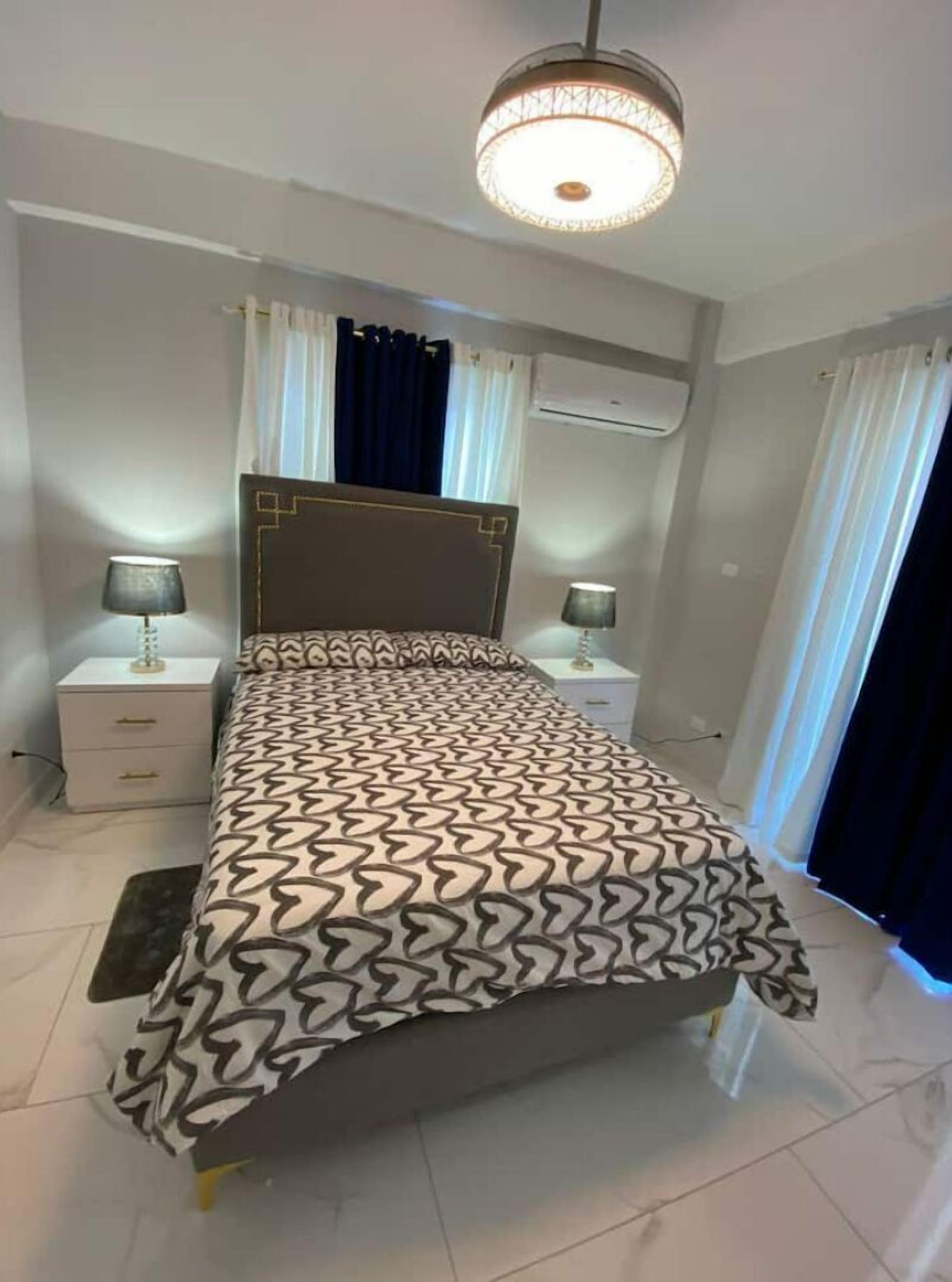 Une chambre à coucher comprenant un lit, deux tables de chevet, un luminaire au plafond et un appareil de climatisation.