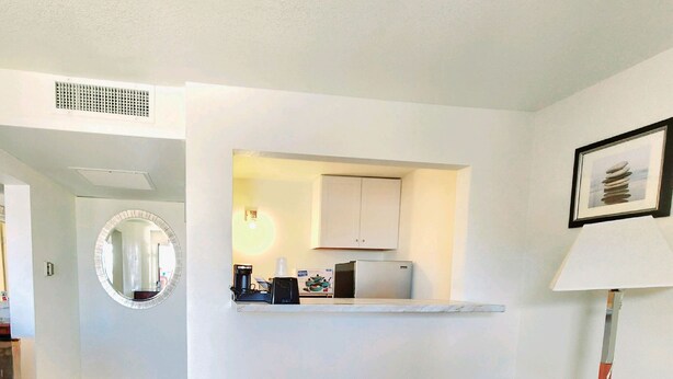 A compact living space with a kitchenette, a round mirror, a small table, and a sofa.