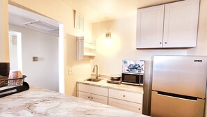 A kitchen with a marble countertop, a stainless steel refrigerator, a microwave, and a sink.