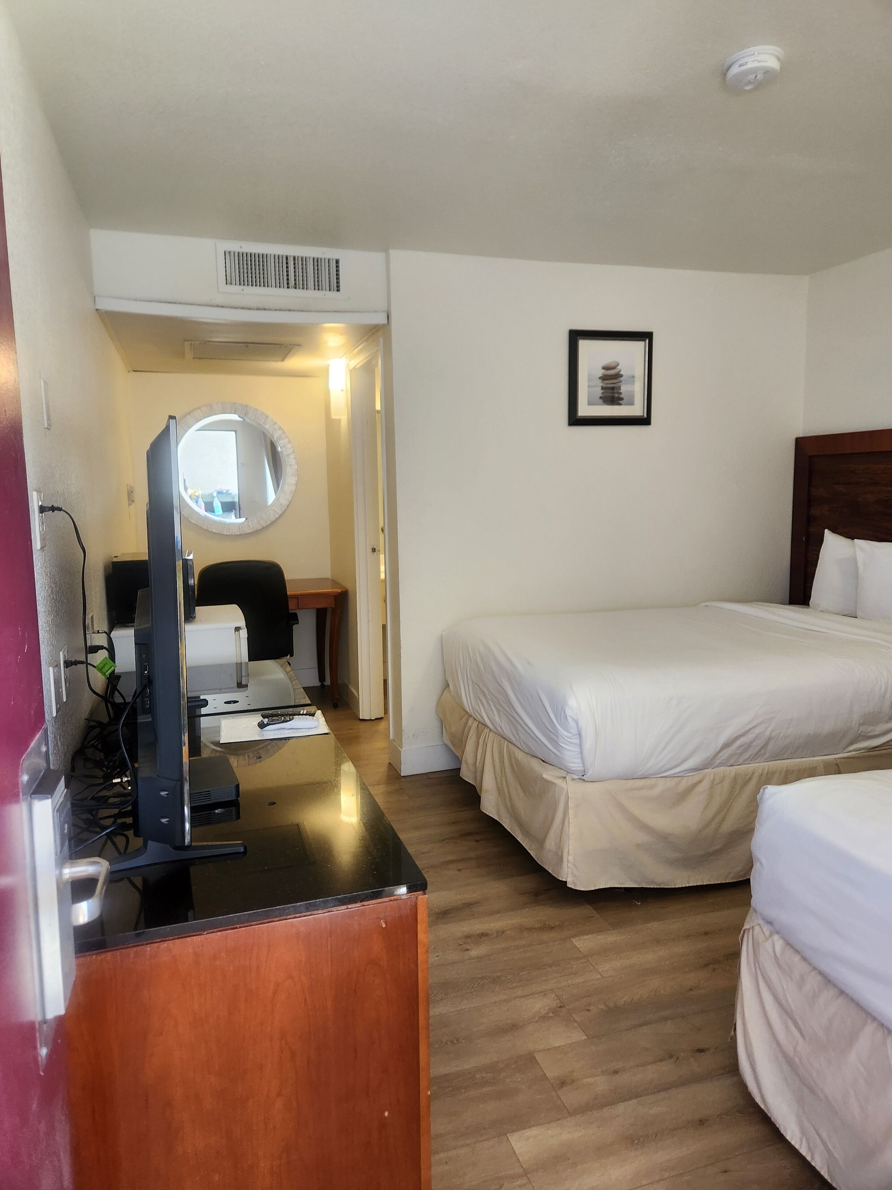 Ein Hotelzimmer mit einem hölzernen Schreibtisch, einem Computer, einem Stuhl, einem Bett und einem gerahmten Bild an der Wand.