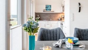 Un espace de repas moderne avec une table dressée pour deux personnes, un vase de fleurs et une vue sur la cuisine.