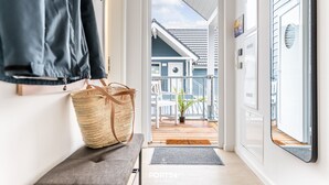 Un couloir mène à un balcon d’où l’on peut admirer une maison. On y trouve un banc sur lequel est posé un panier en osier, ainsi qu’une porte dotée d’un miroir.