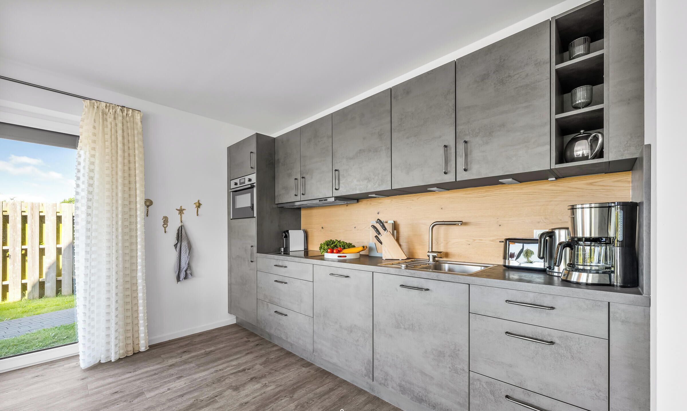 A modern kitchen with grey cabinets, a wooden countertop, a built-in oven, and a coffee maker.