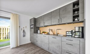 A modern kitchen with grey cabinets, a wooden countertop, a built-in oven, and a coffee maker. - Ferienwohnung Meerverliebt Büsum (Westerdeichstrich)