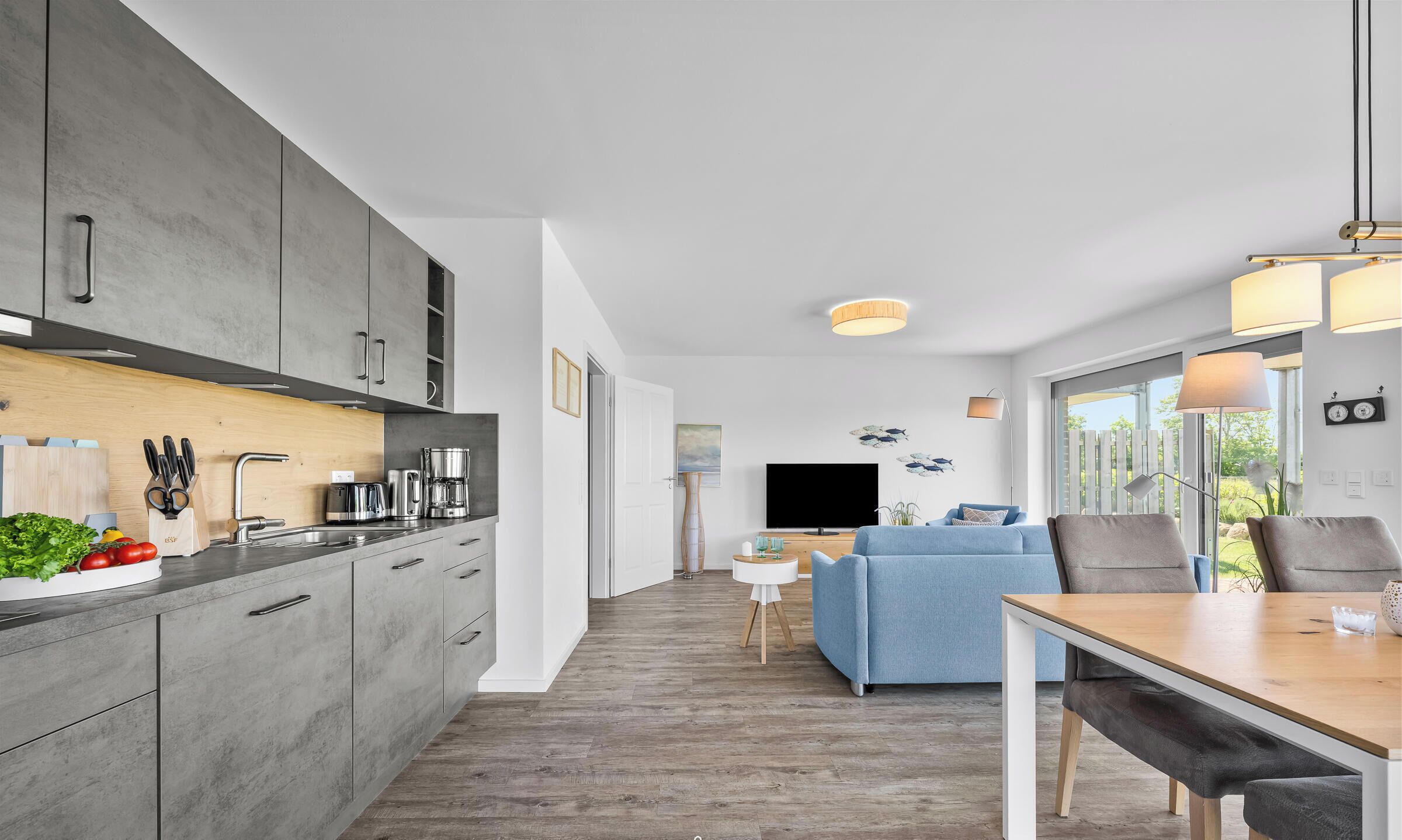 Une cuisine moderne avec des meubles gris, un plan de travail en bois et un coin repas comprenant une table et des chaises.