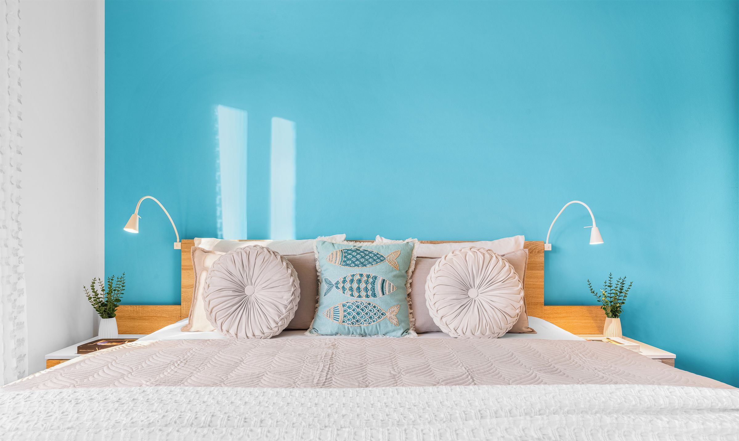 Une chambre avec un mur d’accent bleu, un lit recouvert d’une couvre-lit à motifs, deux lampes de chevet et des coussins décoratifs.
