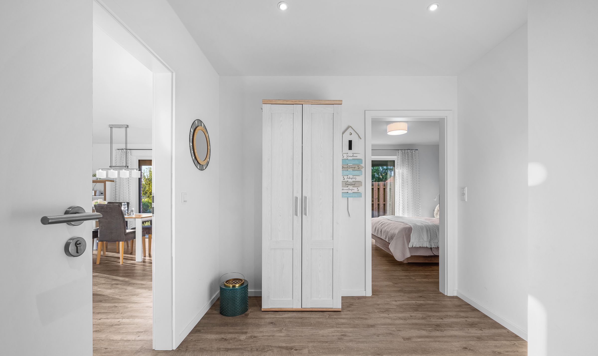 A modern interior with a wooden floor, white walls, a wardrobe, and a dining area with chairs and a table.