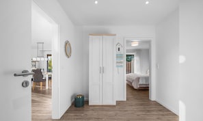 A modern interior with a wooden floor, white walls, a wardrobe, and a dining area with chairs and a table. - Ferienwohnung Meerverliebt Büsum (Westerdeichstrich)