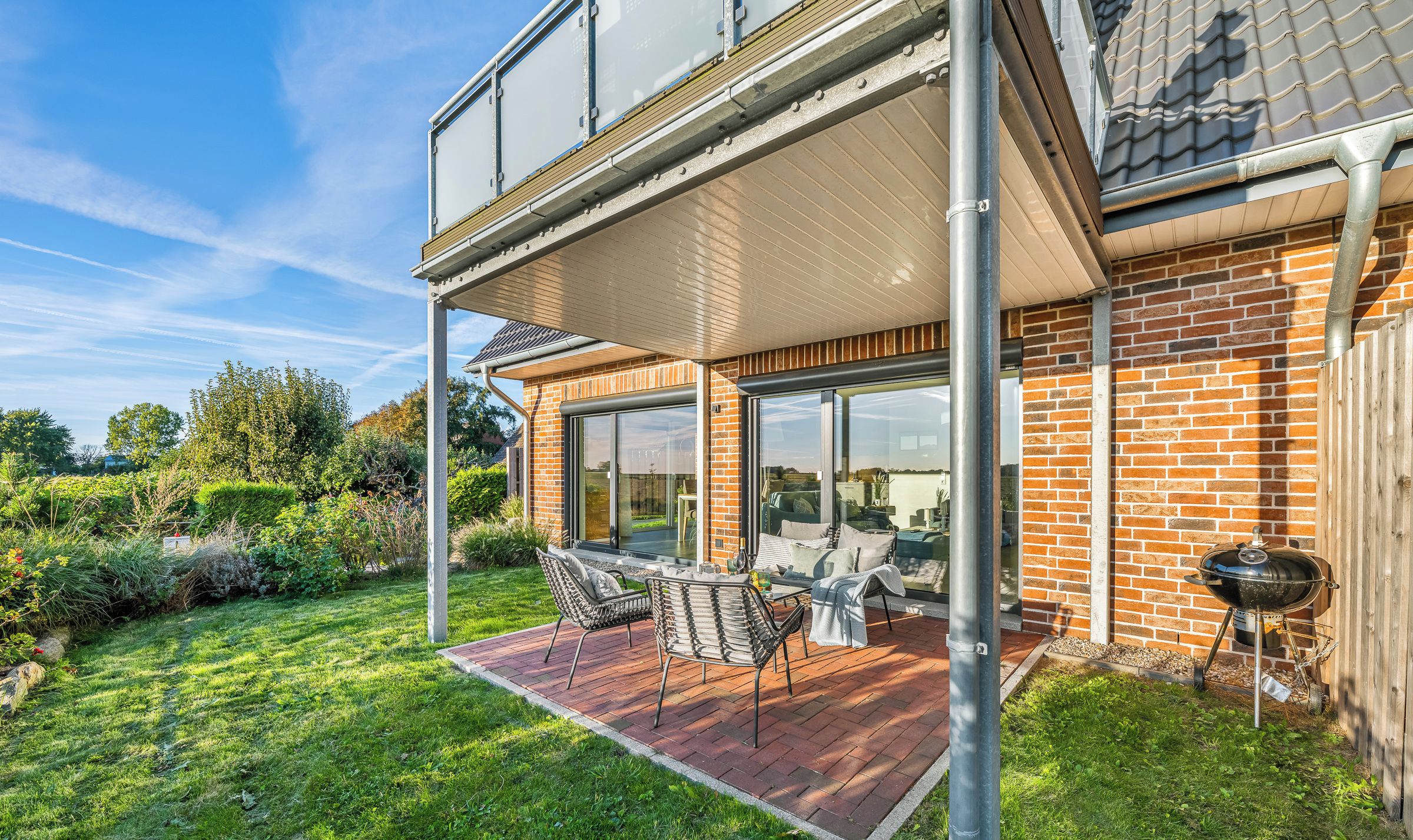 A two-story house with a patio, outdoor seating, and a barbecue grill.