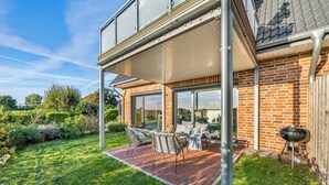Une maison à deux étages dotée d’un patio, d’un espace salon extérieur et d’un barbecue.