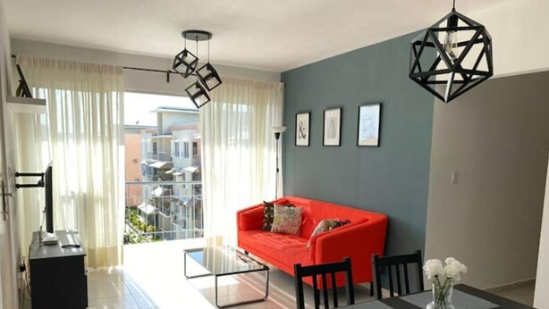Ein modernes Wohnzimmer mit einem roten Sofa, einem Esstisch mit Stühlen und einem Balkon mit Blick auf Gebäude.