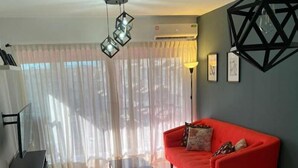 Ein modernes Wohnzimmer mit einem roten Sofa, einem Glastisch und einem Esstisch mit Stühlen. Eine schwarze Pendelleuchte und eine Stehlampe sind ebenfalls vorhanden.
