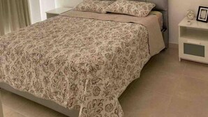 Ein Schlafzimmer mit einer gesteppten Kopfteile, einer gemusterten Bettdecke, einem Nachttisch mit einer Uhr und einem Wandgerät zur Klimatisierung.