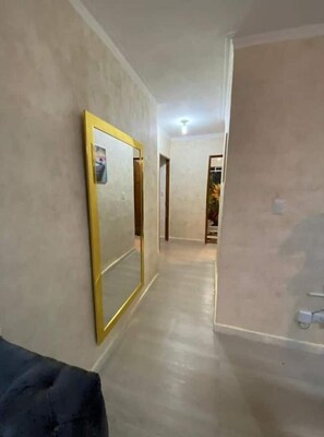 Un couloir avec un grand miroir sur le côté gauche, une porte au fond et une petite table avec un vase sur le côté droit.