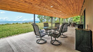 Eine überdachte Terrasse mit Meerblick, ausgestattet mit einem Tisch und Stühlen sowie einer kleinen Sitzecke mit einer Bank und einem Fernseher.