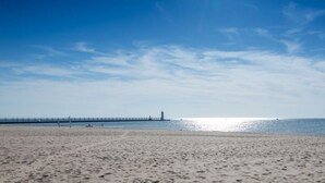 En strand med en moler, der strækker sig ud i vandet, klare himmel og roligt hav.