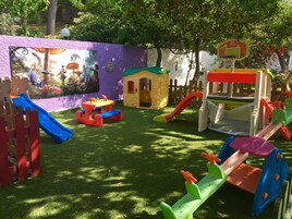 Un área de juegos infantiles con toboganes, una casita y un aro de baloncesto.