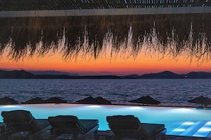 Una piscina infinita con sillas de descanso, vistas al atardecer y sombrillas de paja.