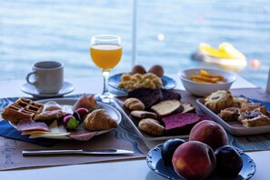A breakfast table with various foods and a glass of orange juice. - Venus Beach Hotel (Karystos)