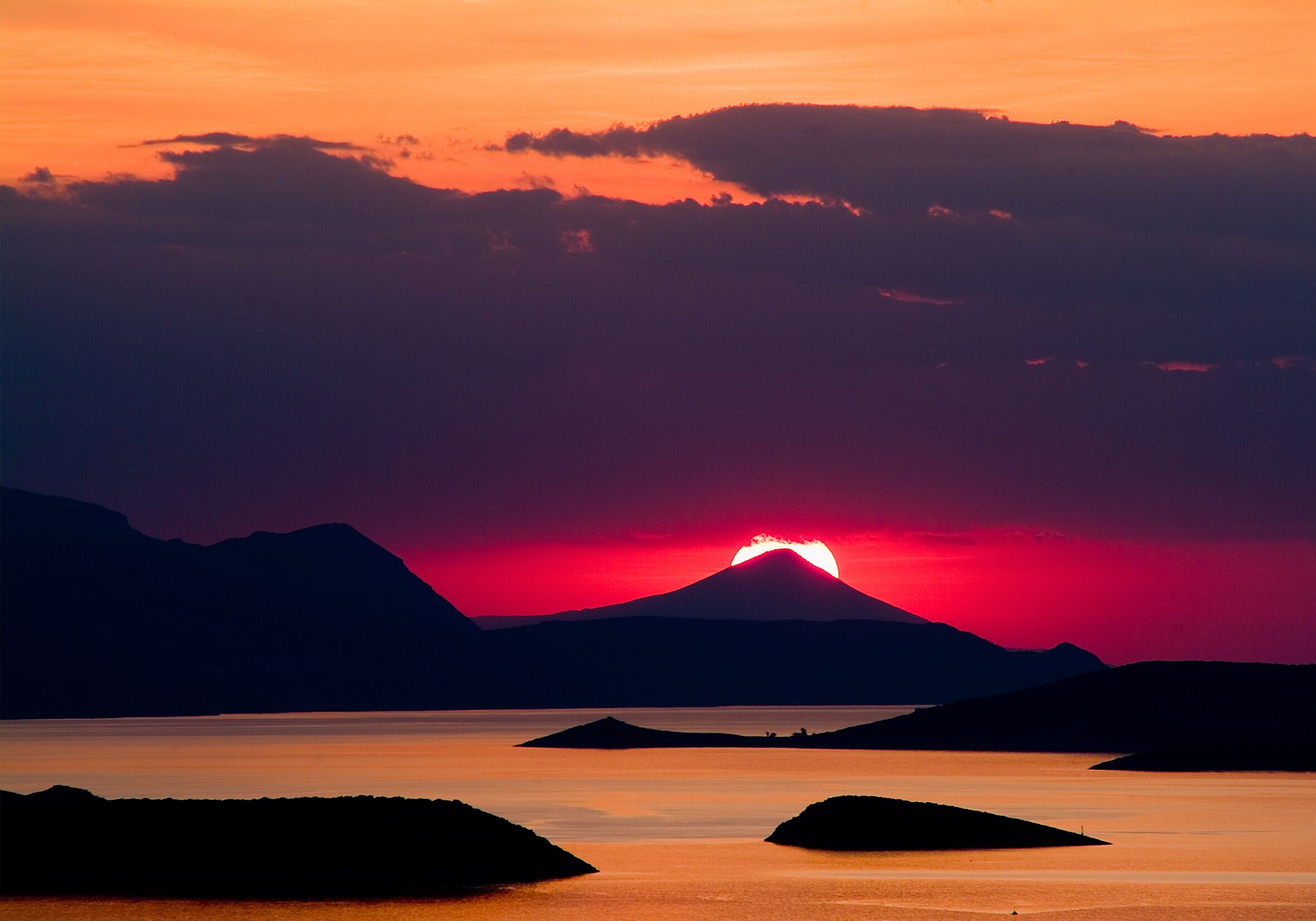 A sunset over a calm lake with mountains in the background.