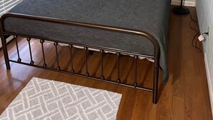 A neatly made bed with a metal frame, a patterned bedspread, and a decorative wall piece above it. - X Marks the Spot (Purple) (Santa Claus)