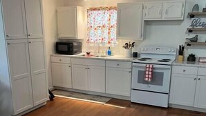 A kitchen with white cabinets, a microwave, a stove, and a window with a floral curtain. - X Marks the Spot (Purple) (Santa Claus)