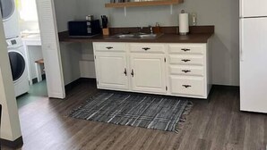 Une cuisine compacte avec des meubles blancs, un plan de travail en bois et un évier encastré. On y trouve deux éléments de décoration murale et un réfrigérateur blanc.