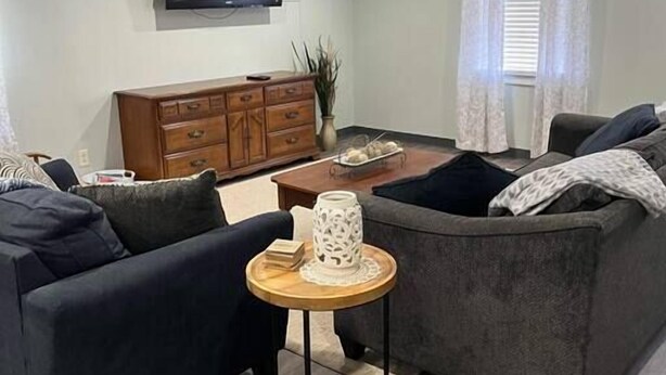 Un salon avec deux canapés, une petite table en bois, un téléviseur fixé au mur et une fenêtre avec des rideaux.