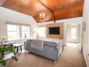 A cozy living room with a grey sofa, wooden ceiling, and a flat-screen TV mounted on the wall. - The Flat (Carlisle)