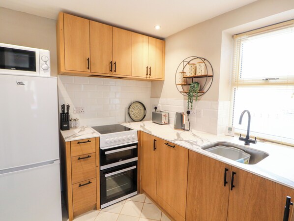 A modern kitchen with wooden cabinets, a built-in oven, a microwave, and a sink. - The Flat (Carlisle)