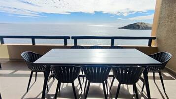 A balcony with a table and chairs, overlooking a body of water and a distant island.