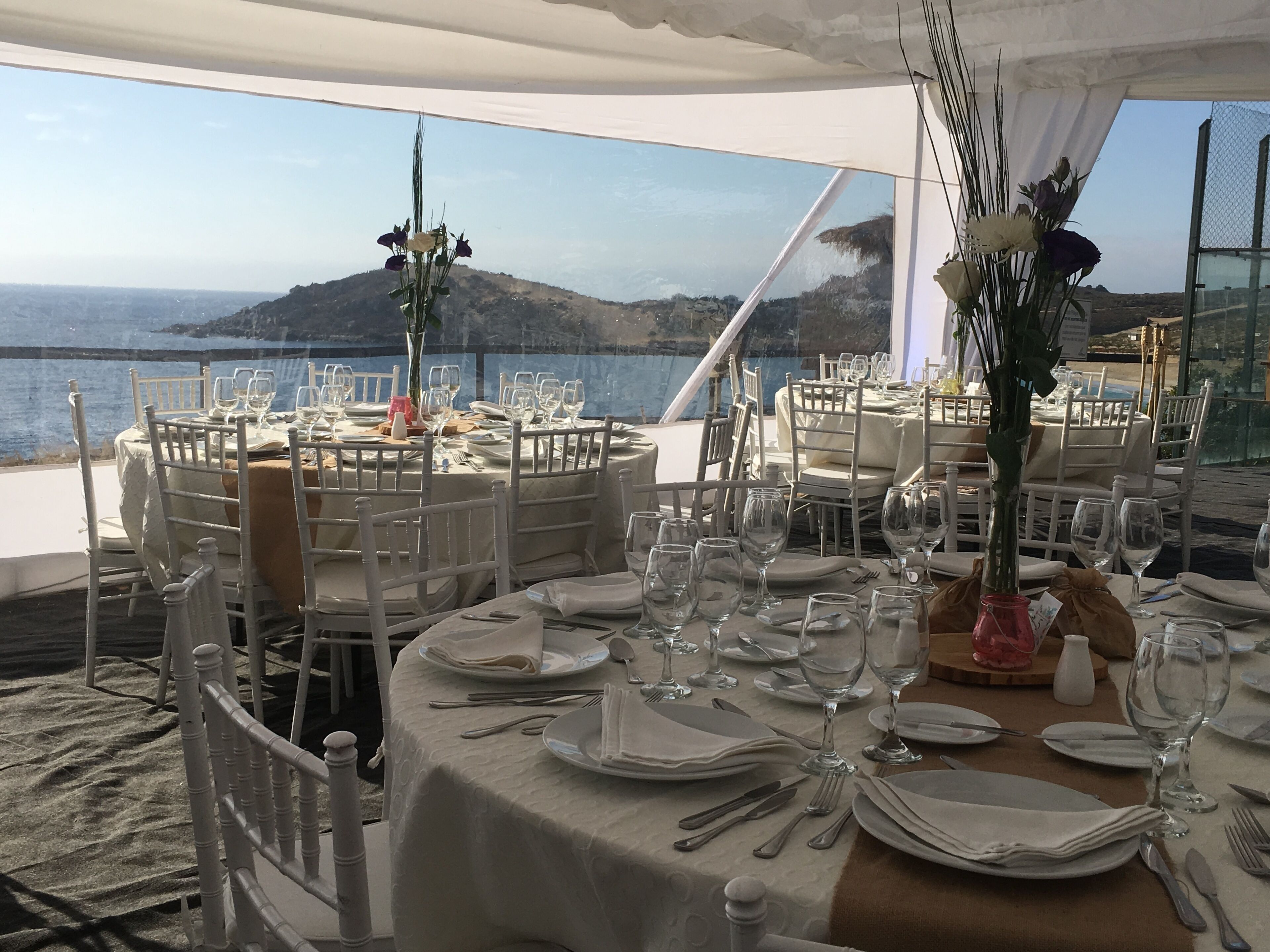 A tented dining area with round tables set for a meal, overlooking a coastal landscape.