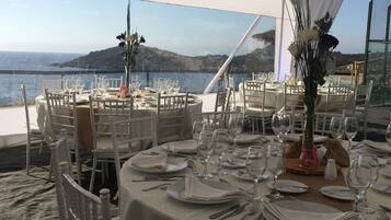 A tented dining area with round tables set for a meal, overlooking a coastal landscape.