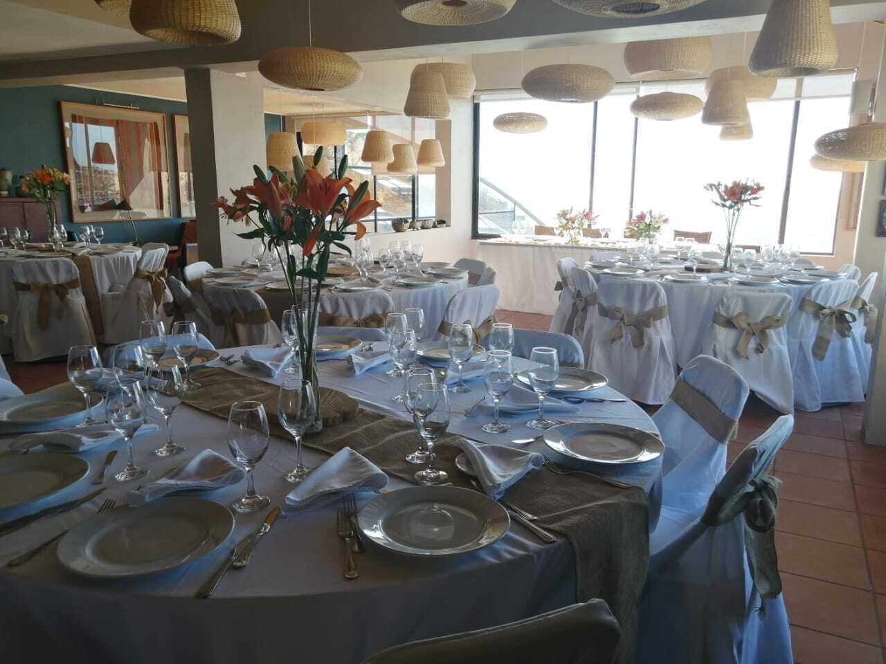 Un comedor con mesas redondas dispuestas para una comida, con manteles blancos, cubertería y copas.