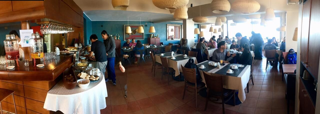 A restaurant with multiple dining tables and chairs, a bar area with a drink dispenser, and a counter with food and condiments.