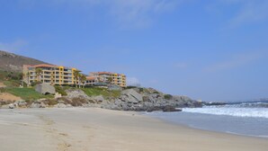 Ein Strandhotel mit mehreren Balkonen, einer felsigen Küstenlinie und brechenden Wellen.