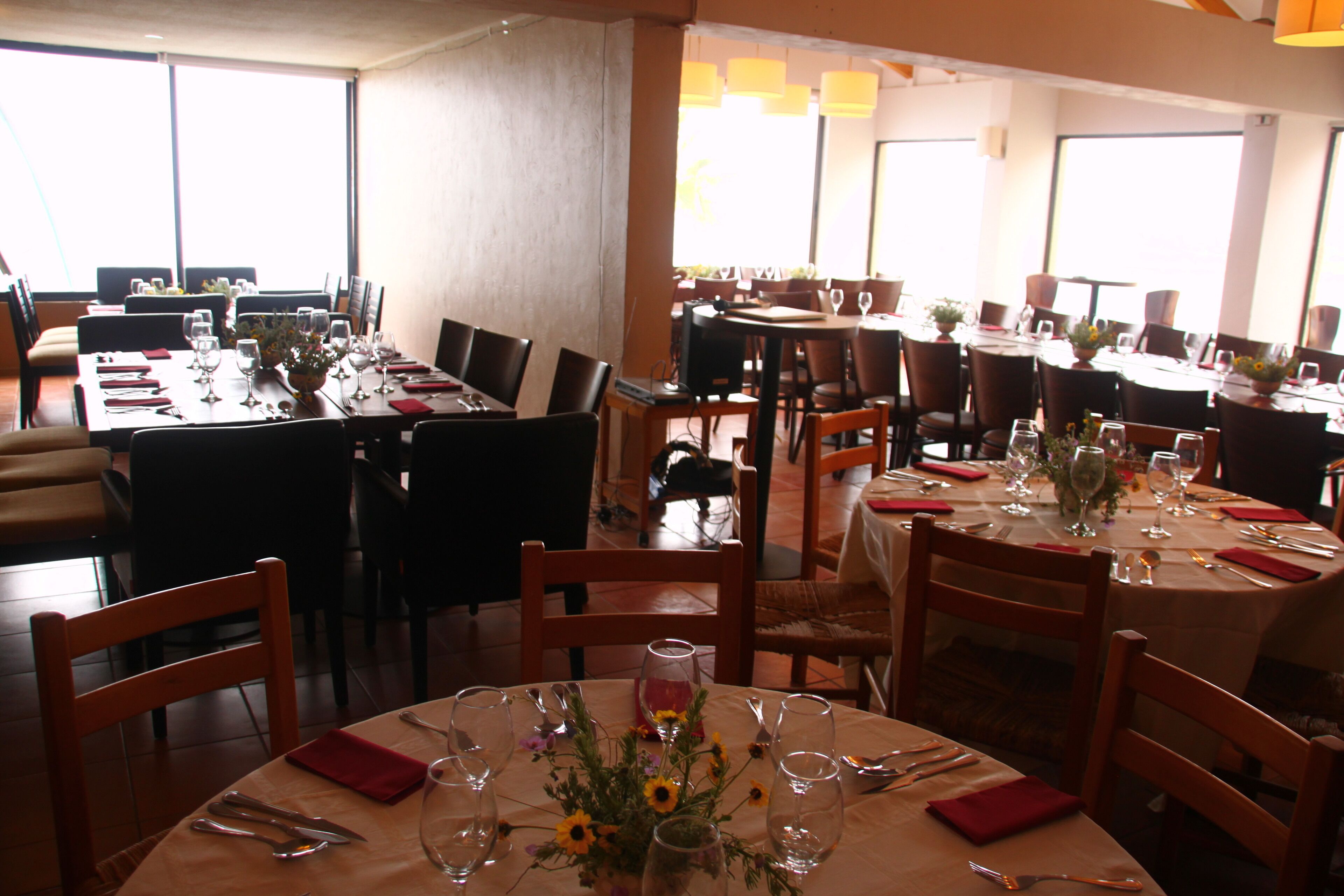 Un restaurant doté de plusieurs tables, chacune agrémentée de serviettes rouges, de verres à vin et de compositions florales.