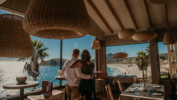 Ein Paar umarmt in einem Restaurant mit großen Fenstern und Blick auf den Strand.