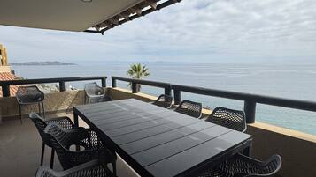 An outdoor terrace with a table and chairs, overlooking a body of water and a distant coastline.