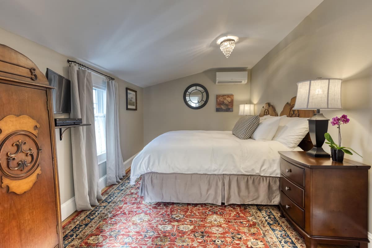 A bedroom with a large bed, a wooden dresser, a television, and a chandelier.
