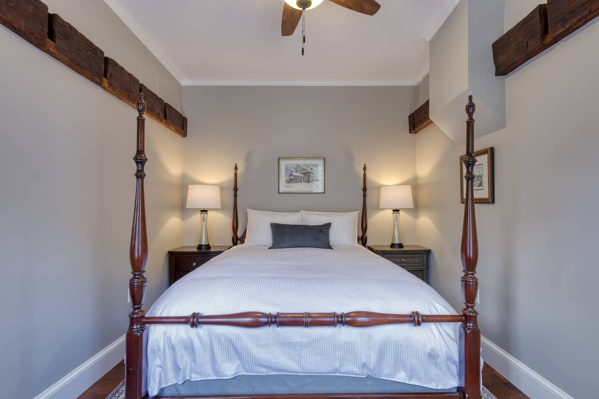 A four-poster bed with a wooden frame, white bedding, and two bedside lamps.