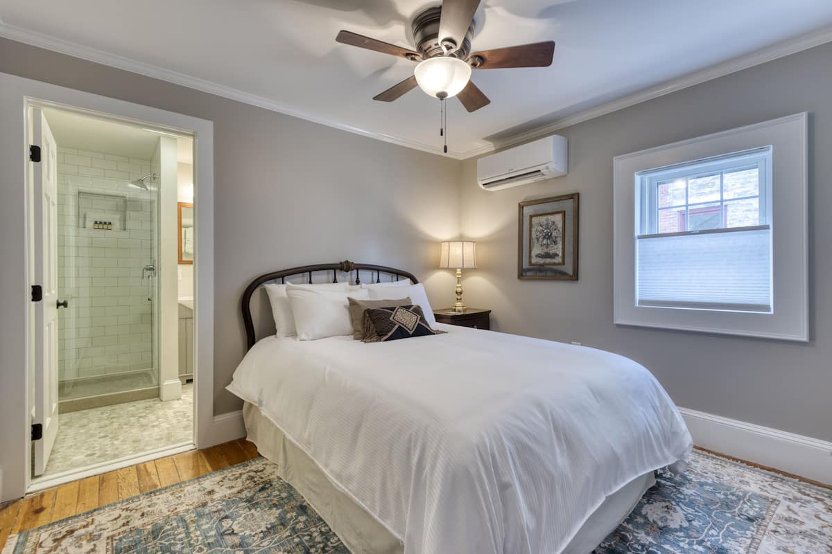 A bedroom with a bed, a ceiling fan, a window, and an air conditioning unit.