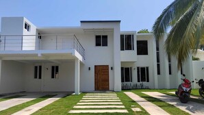 A modern two-story house with a flat roof, a wooden front door, and a balcony on the upper floor. - Hermosa casa de mar (Escuintla)