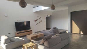 A modern living room with a large flat-screen TV, a wooden coffee table, a grey sofa, and a small wooden stool. - Hermosa casa de mar (Escuintla)